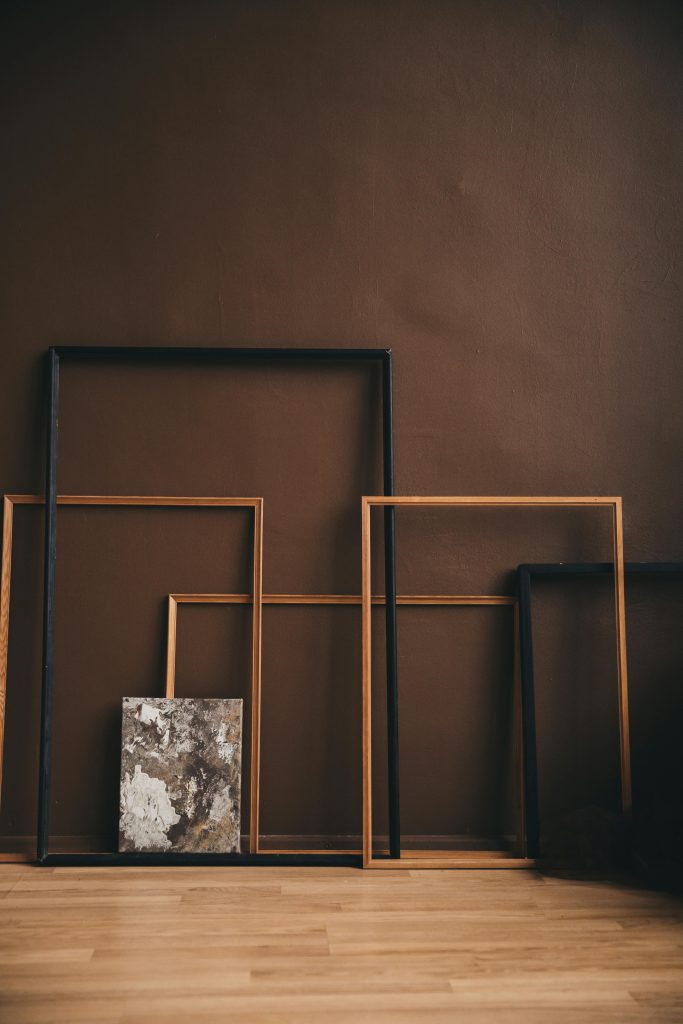 Minimalist wooden and metal frames leaning against a rustic wall in an art studio.
