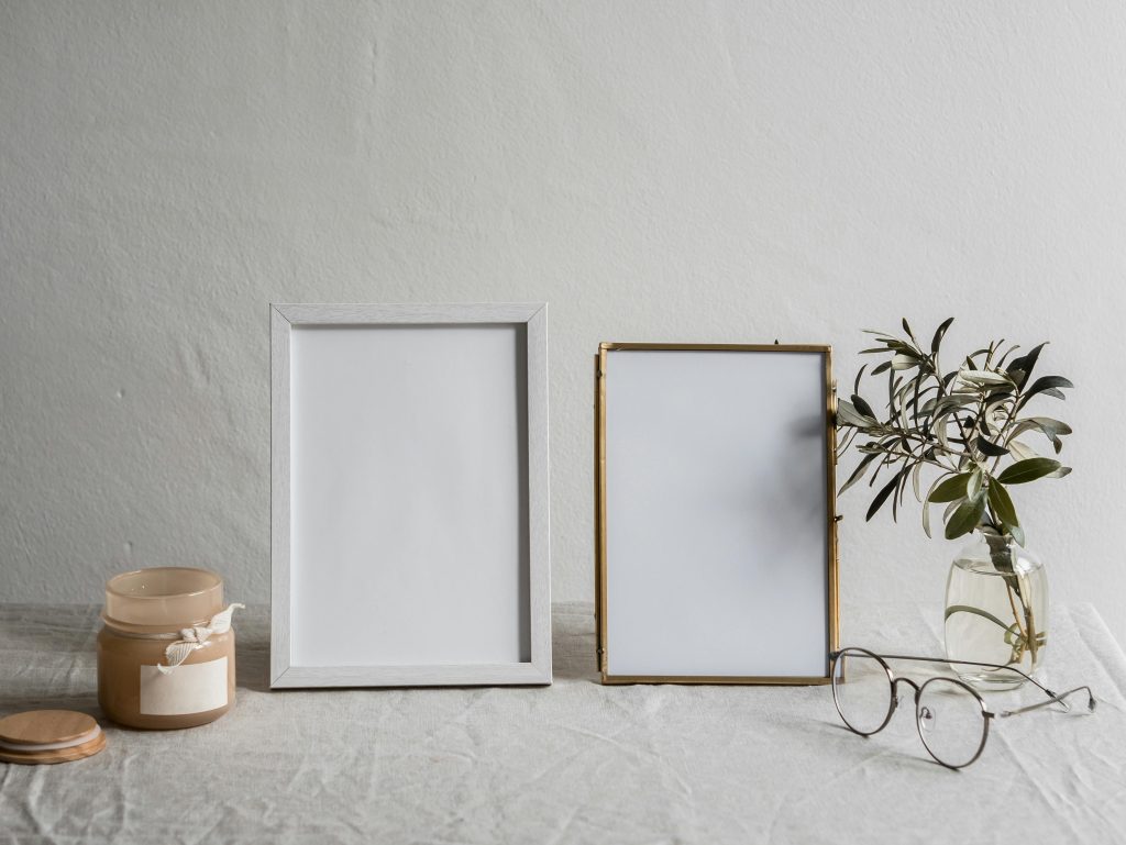 A serene minimalist still life featuring blank frames, glasses, and a candle on a neutral background.